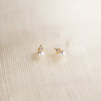 Raindrop Pearl Studs: gold and pearl earrings with small crystals, shown on a textured cream fabric background.