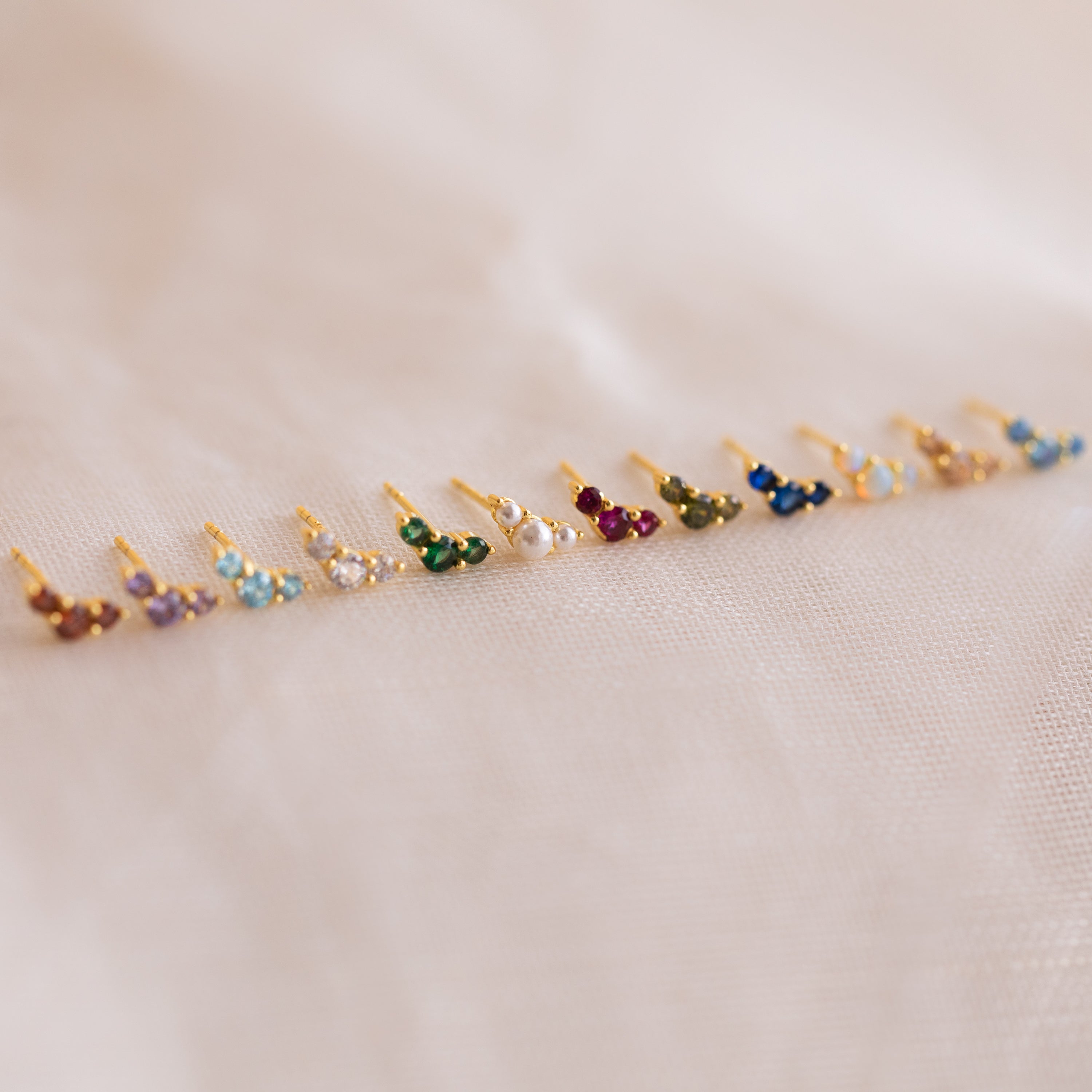 Bella Topaz Studs—gold earrings featuring vibrant stones in a neat row, displayed on soft light fabric. A timeless accessory and perfect gift for mothers and daughters.