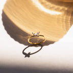 The Mariposa Diamond Ring, featuring a gold butterfly design, casts an elegant shadow on a light surface under bright sunlight.