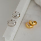 The Olivia Hoops in Sterling Silver—chunky, modern earrings—are displayed on a white marble surface, perfect for adding a contemporary touch to any outfit.