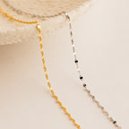 The Josephine Chain Bracelet, a delicate gold and silver beaded design, is displayed draped over a textured white ceramic dish on a neutral background.