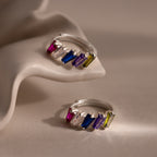 Two Multiple Tapered Birthstone Huggies in Sterling Silver, featuring rectangular multicolored gemstones, are displayed on a soft beige, sculptural surface.
