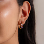 Close-up of a woman’s ear wearing the Multiple Tapered Birthstone Huggies, gold hoop earrings with red and purple accents that bring bold, contemporary flair to modern statement jewelry.