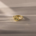 The North Star Birthstone Signet Ring, featuring a hammered gold finish and a central blue zircon for December birthdays, rests on a soft beige surface.