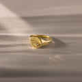 The North Star Birthstone Signet Ring in Diamond (April) features a round, flat top with a diamond accent, shown on a soft beige surface—an elegant and symbolic jewelry piece.