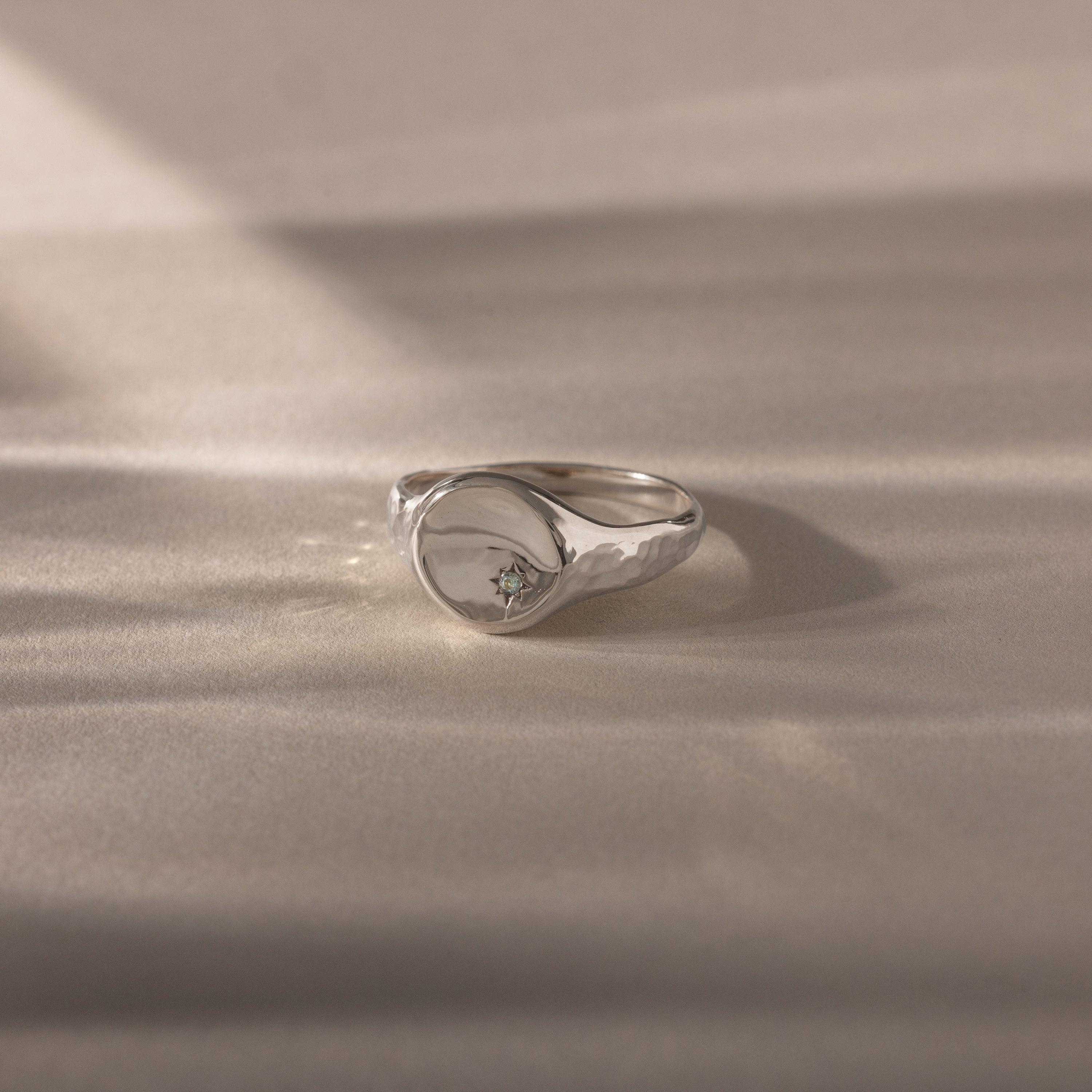 The North Star Aquamarine Signet Ring is a vintage-inspired silver ring featuring a small aquamarine gemstone, shown on a soft beige surface with gentle lighting—a perfect piece of symbolic jewelry.