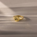 The North Star Birthstone Signet Ring in Topaz (November) features a small star-shaped engraving and is displayed on a soft, beige surface.