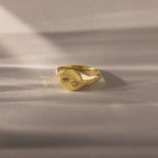 North Star Birthstone Signet Ring in Pink Tourmaline (October) with a hammered band and small gemstone, shown on a smooth neutral surface in soft lighting.