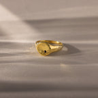 The North Star Birthstone Signet Ring, featuring an onyx center stone, is a symbolic gold ring displayed elegantly on a light, textured surface.