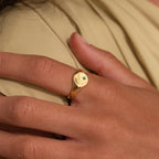 A hand wearing the North Star Birthstone Signet Ring with a small green gemstone on the index finger—this elegant piece adds a touch of sophistication and personal significance.