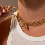 Close-up of a person wearing two gold necklaces, including one with the Pavé Pink Tourmaline Charm Spacer, paired with a white ribbed tank top—perfect for showcasing stylish birthstone jewelry.