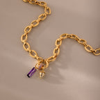 Skinny Baguette Sapphire Charm gold necklace with a purple baguette-cut pendant and a small strawberry birthstone charm, shown on a beige background.