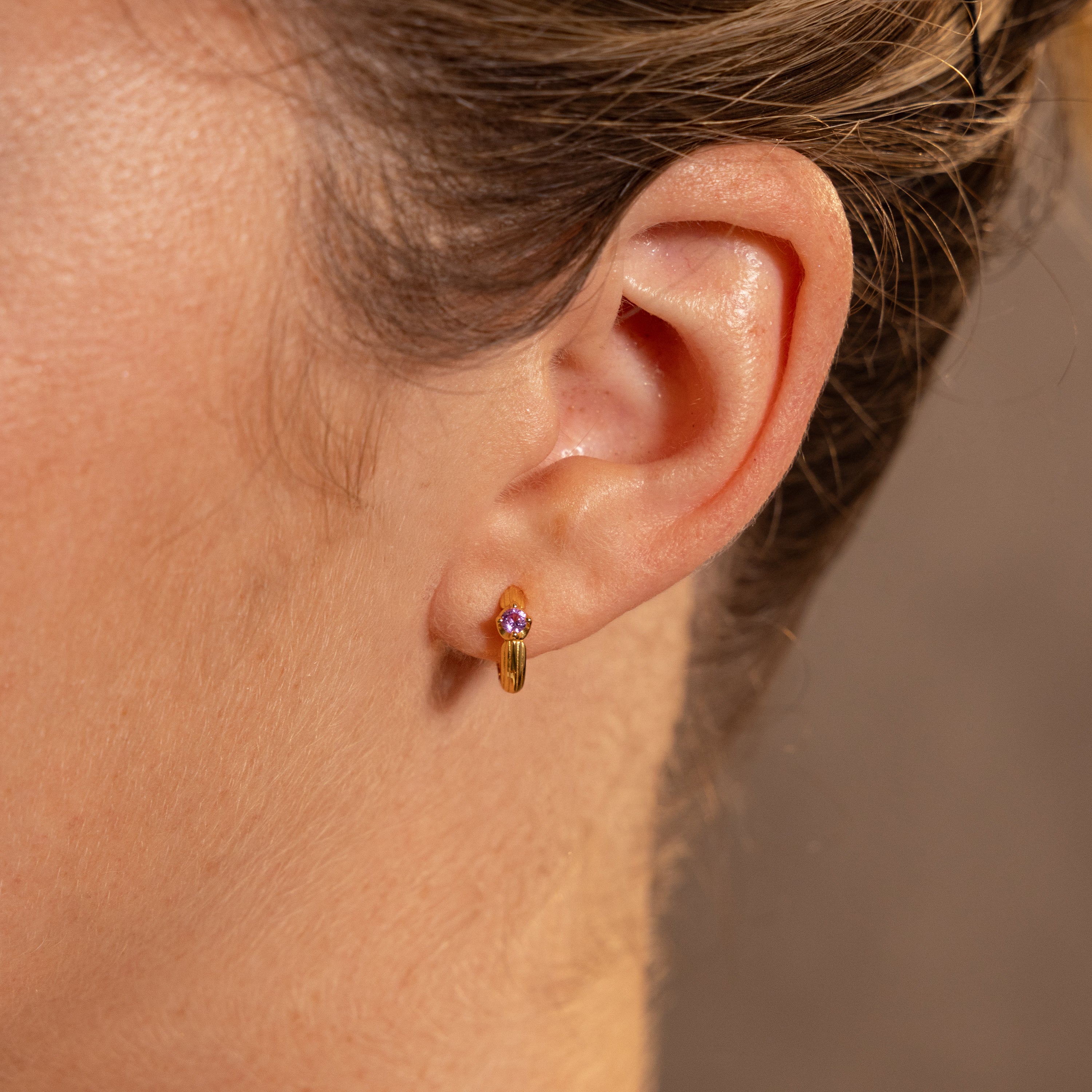 Close-up of a womans ear wearing Ribbed Topaz Huggies, featuring a small gold hoop with a vibrant topaz stone—perfect as a meaningful gift.