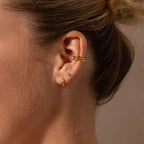 Close-up of a womans ear wearing three gold hoop earrings, including the Ribbed Alexandrite Huggies, an ear cuff, and her hair tied back.