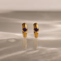 Ribbed Amethyst Huggies—gold hoop earrings with purple gemstones, displayed upright on a marbled surface with soft lighting—perfect for anyone who loves unique birthstone jewelry.
