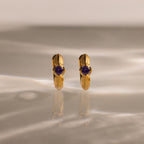 Ribbed Amethyst Huggies—gold hoop earrings with purple gemstones, displayed upright on a marbled surface with soft lighting—perfect for anyone who loves unique birthstone jewelry.