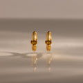 A pair of Ribbed Topaz Huggies gold hoop earrings with yellow gemstones displayed on a reflective, neutral surface.
