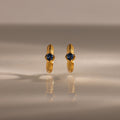 The Ribbed Blue Zircon Huggies, gold hoop earrings with blue zircon centers, are shown on a reflective surface, making this personalized jewelry sparkle.