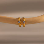 Ribbed Peridot Huggies—small gold hoop earrings with a single peridot gemstone, shown on a smooth wooden rod—ideal for lovers of personalized jewelry or classic huggie styles.