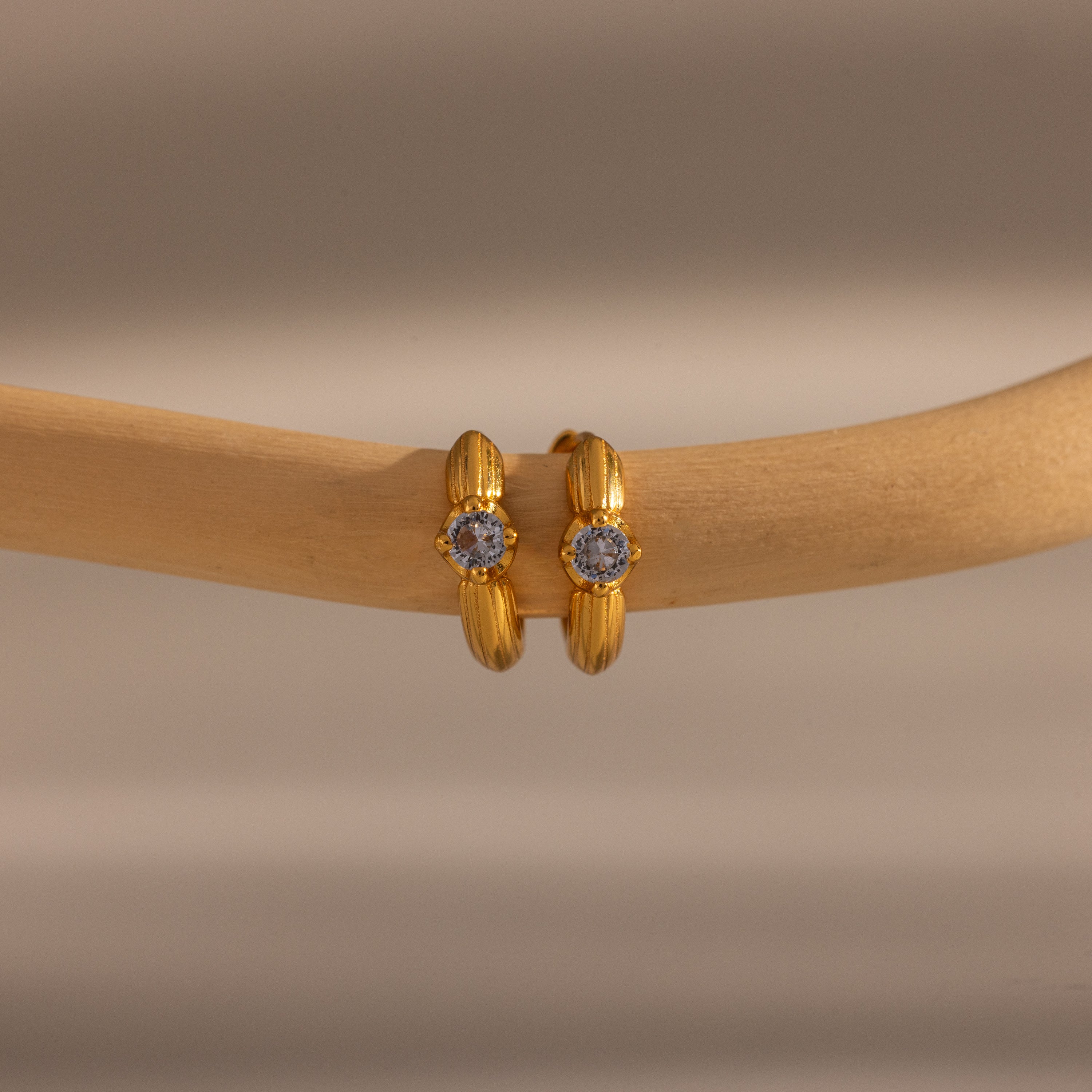 Close-up of two Ribbed Sapphire Huggies gold hoop earrings, each adorned with a small sapphire gemstone and displayed on a beige wooden rod. Perfect for lovers of personalized jewelry.