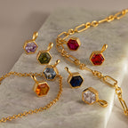 The Hexagon Garnet Charm is a gold geometric jewelry piece with a faceted garnet birthstone, displayed on a marble surface.