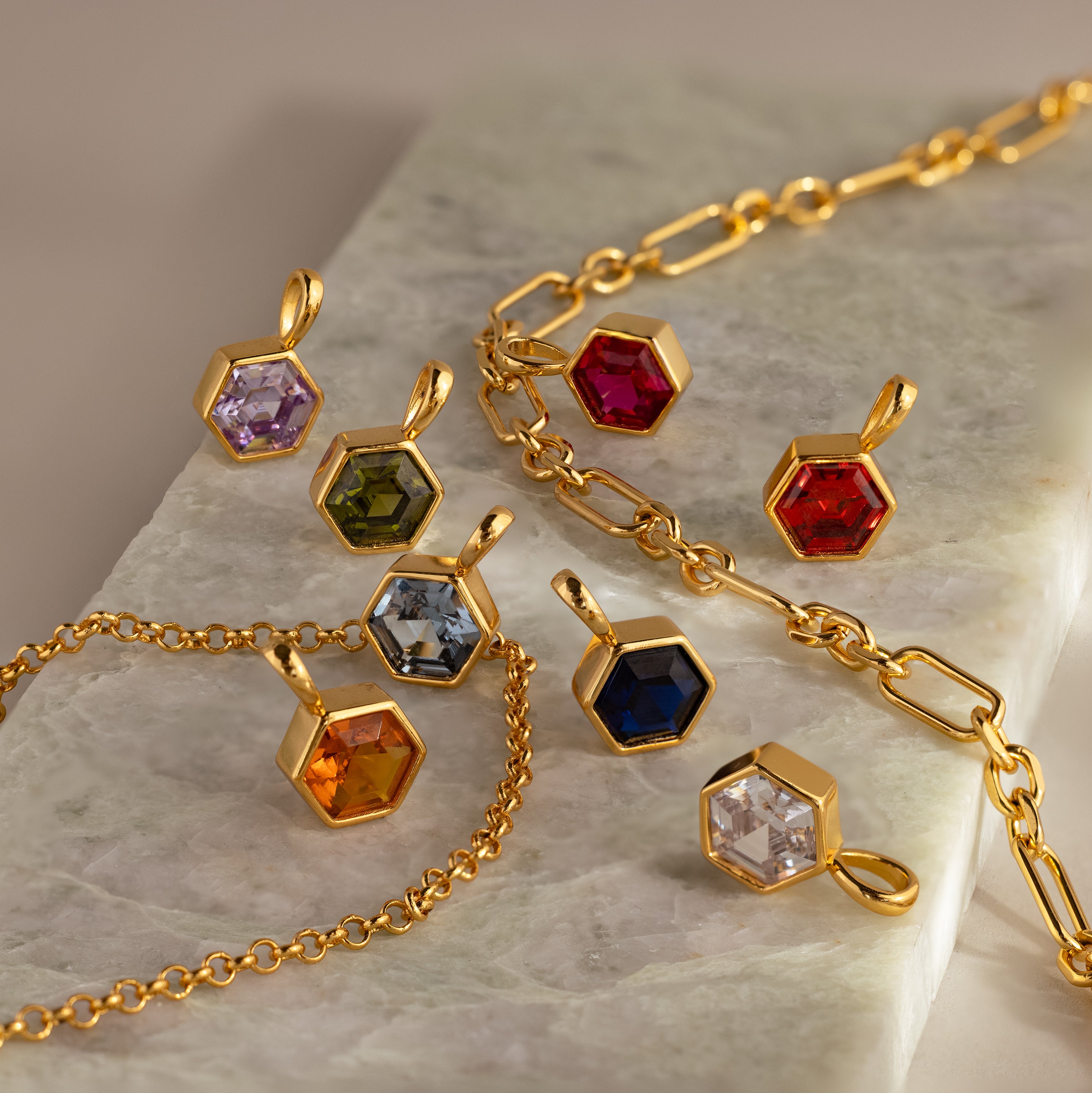 The Hexagon Garnet Charm is a gold geometric jewelry piece with a faceted garnet birthstone, displayed on a marble surface.