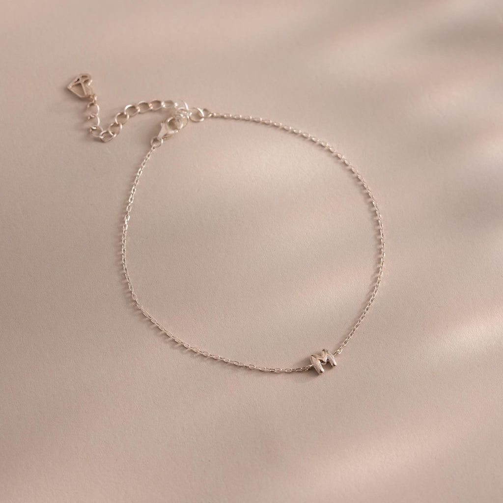 The Bubble Initial Bracelet is a delicate silver personalized piece featuring an initial charm, ideal for everyday wear and beautifully displayed on a light beige surface.