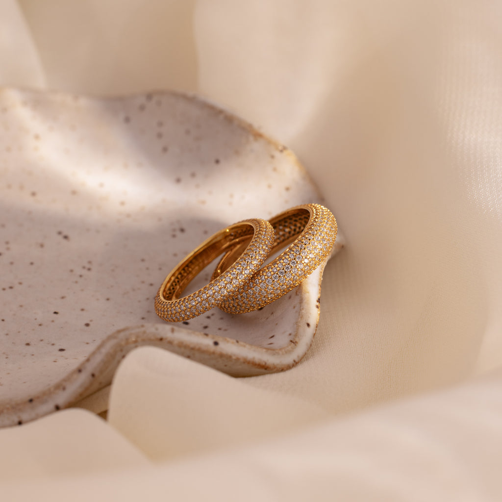 Two Pave Stacking Rings with shimmering diamonds are displayed on a speckled ceramic dish, accented by soft beige fabric.