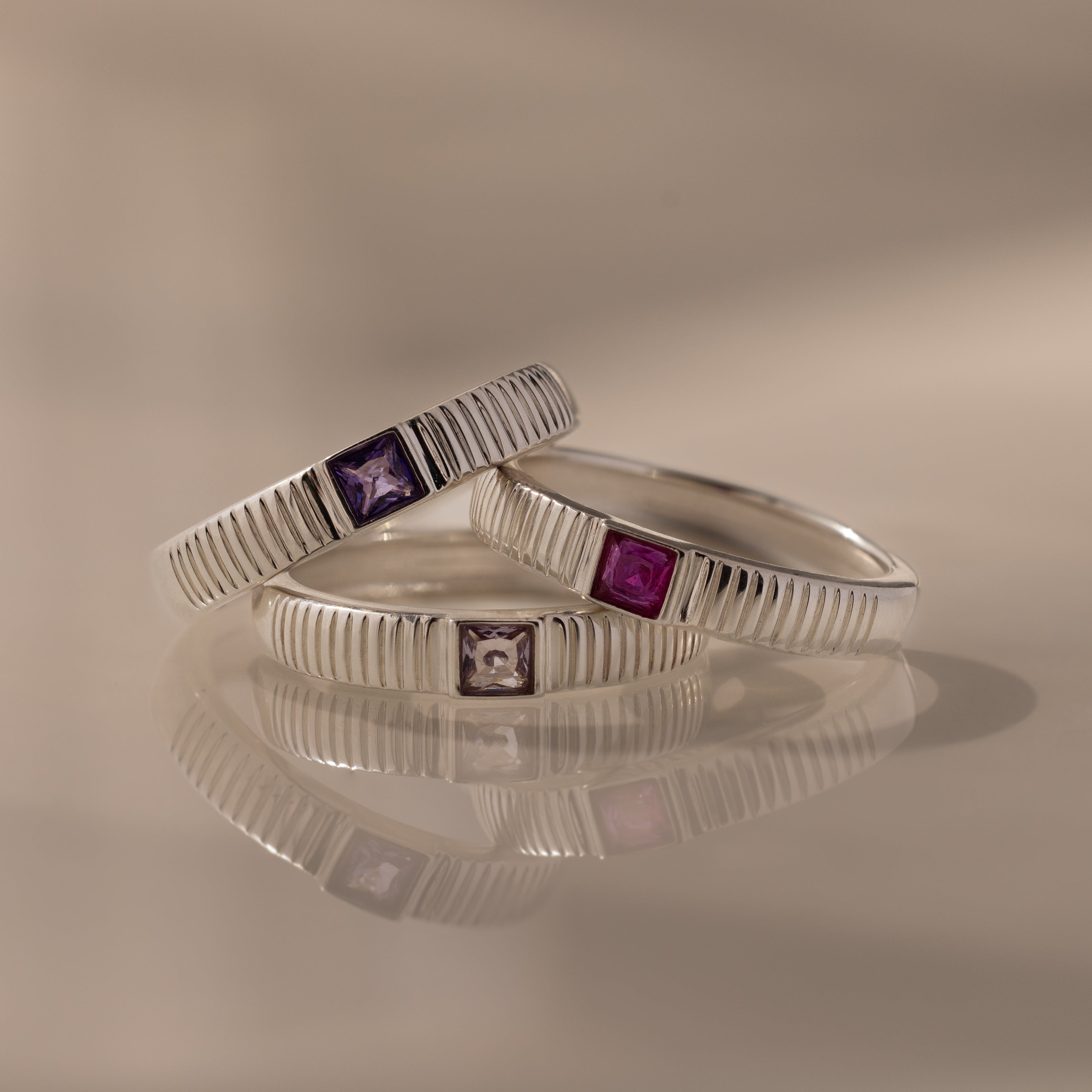 The Ribbed Amethyst Band is a stylish silver stacking ring featuring a square purple gemstone, perfect for adding birthstone elegance to any look.