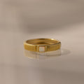 The Ribbed Opal Band features a gold ribbed band and a small rectangular opal stone, beautifully reflected on a smooth surface.