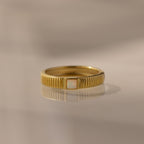 The Ribbed Opal Band features a gold ribbed band and a small rectangular opal stone, beautifully reflected on a smooth surface.
