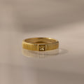 The Ribbed Topaz Band features a ribbed gold band and a single square-cut topaz, beautifully reflected on a smooth surface.