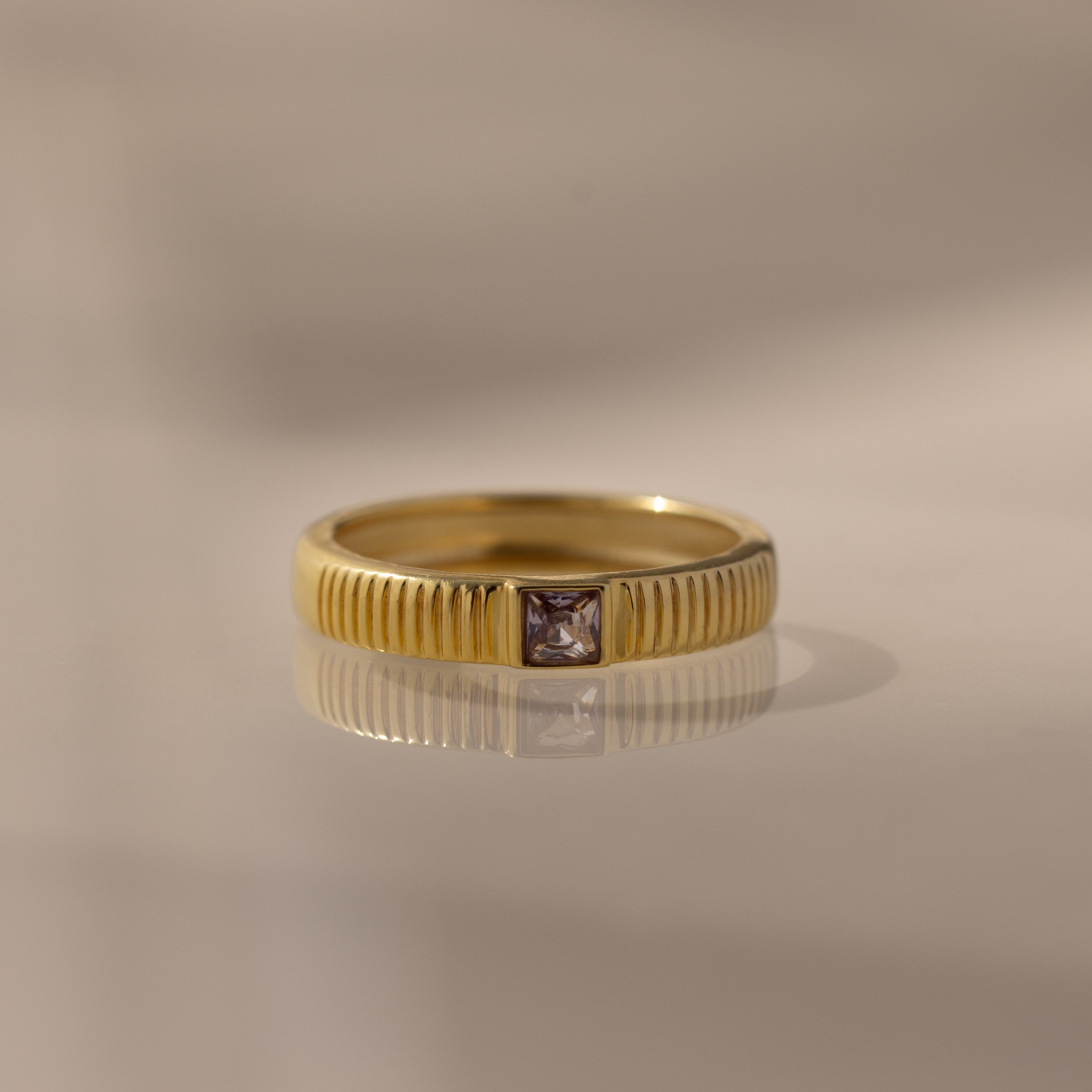 The Ribbed Alexandrite Band showcases a square-cut alexandrite center stone, offering elegant birthstone style against any backdrop.