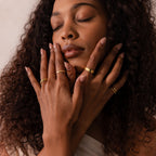 Woman with curly hair wearing a Ribbed Name Ring, eyes closed, gently touching her face with both hands.