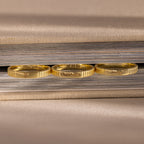 Three gold rings with engraved messages—including a custom piece and the Ribbed Name Ring in 18K Gold—rest upright against the edge of a closed book.