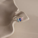 The Multiple Marquise Birthstone Ring in Sterling Silver features three marquise-cut stones—light blue, dark blue, and pink—on a wavy, beige surface. A personalized jewelry piece ideal for milestone gifts or special occasions.