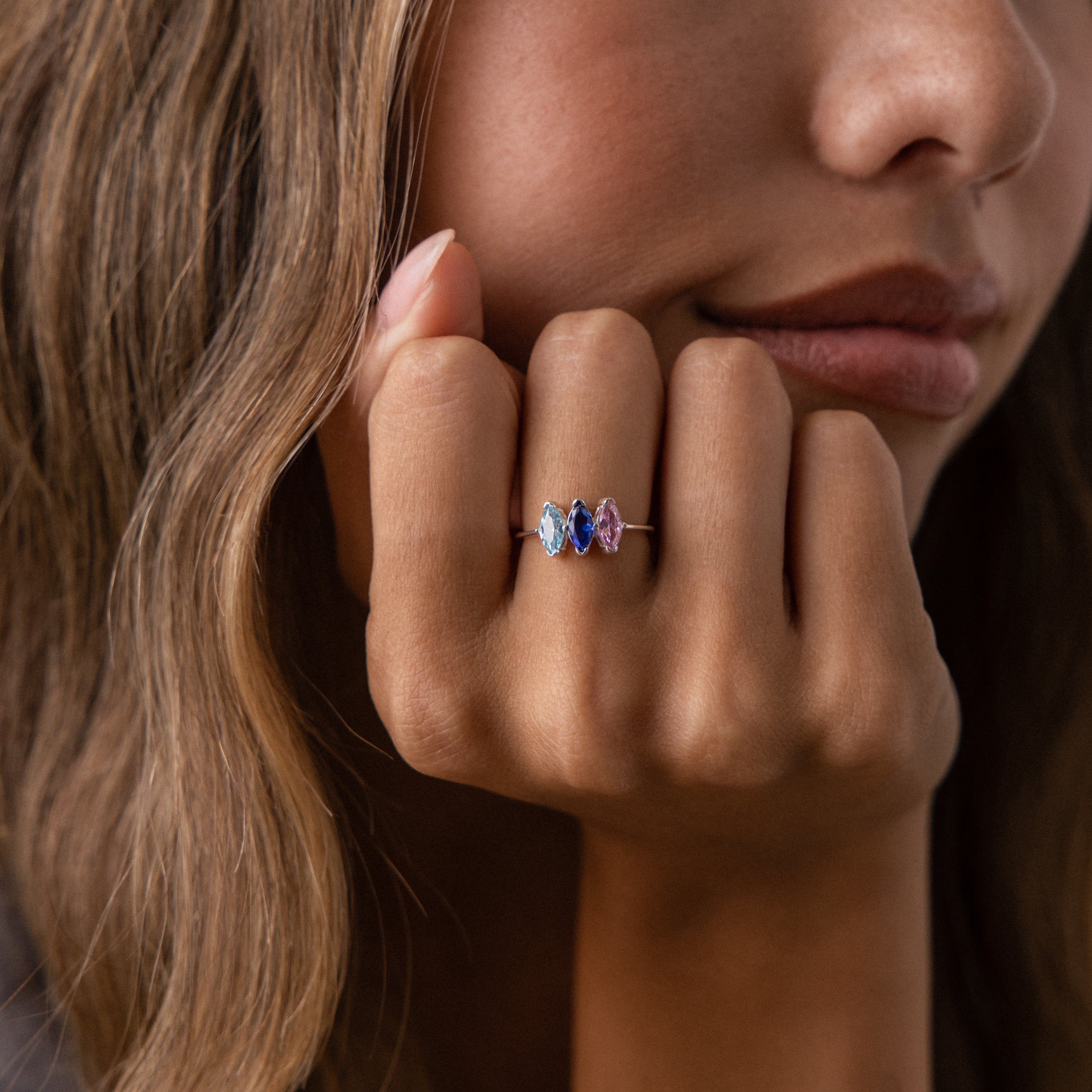 A woman with wavy hair rests her chin on her hand, showcasing the Multiple Marquise Birthstone Ring featuring blue, purple, and pink stones.