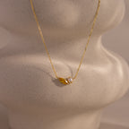 The Marquise Topaz & Pearl Necklace features a gold chain with a small leaf charm and pearl pendant, displayed on a textured light surface. This elegant necklace can be customized as a unique birthstone piece for a personal touch.