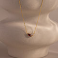 The Marquise Garnet & Pearl Necklace features a marquise-shaped garnet birthstone and a small pearl pendant, elegantly displayed on a textured beige bust.