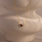The Marquise Garnet & Pearl Necklace features a marquise-shaped garnet birthstone and a small pearl pendant, elegantly displayed on a textured beige bust.