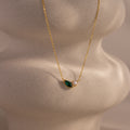 The Marquise Emerald & Pearl Necklace features a green marquise emerald birthstone and a delicate pearl pendant, displayed on a textured, sculpted surface.