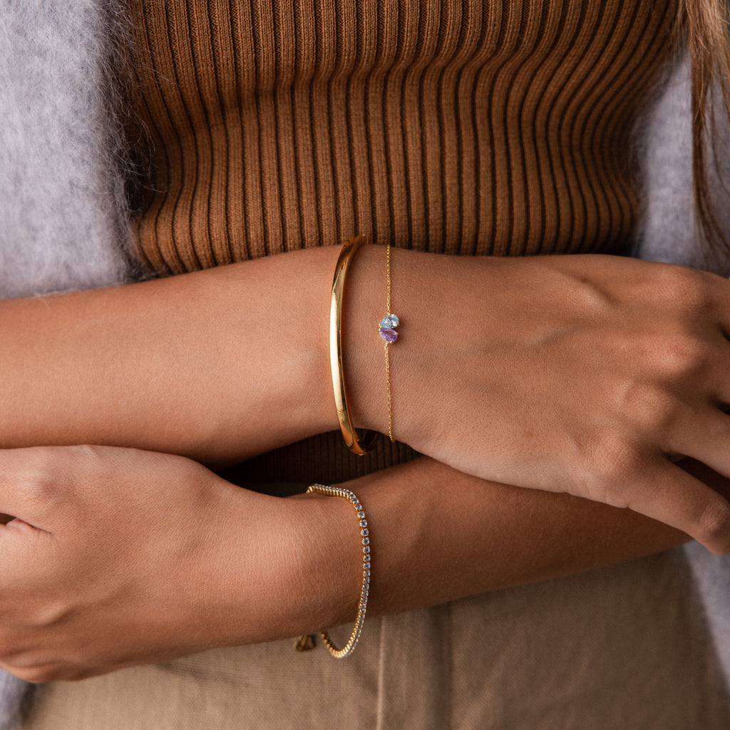 Close-up of crossed arms wearing the Toi et Moi Teardrop Heart Bracelet over a brown ribbed top and beige pants.