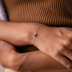 The Toi et Moi Teardrop Heart Bracelet, featuring a delicate silver teardrop heart and a small blue and gold charm, adorns a person’s wrist.