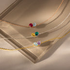 The Toi et Moi Teardrop Heart Bracelet features delicate chains and colorful teardrop heart pendants, elegantly displayed on a beige glass surface.