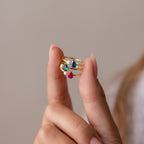 A hand displays the Teardrop Birthstone & Pearl Ring, featuring colorful gemstone and pearl accents, against a neutral background to showcase its elegant design.