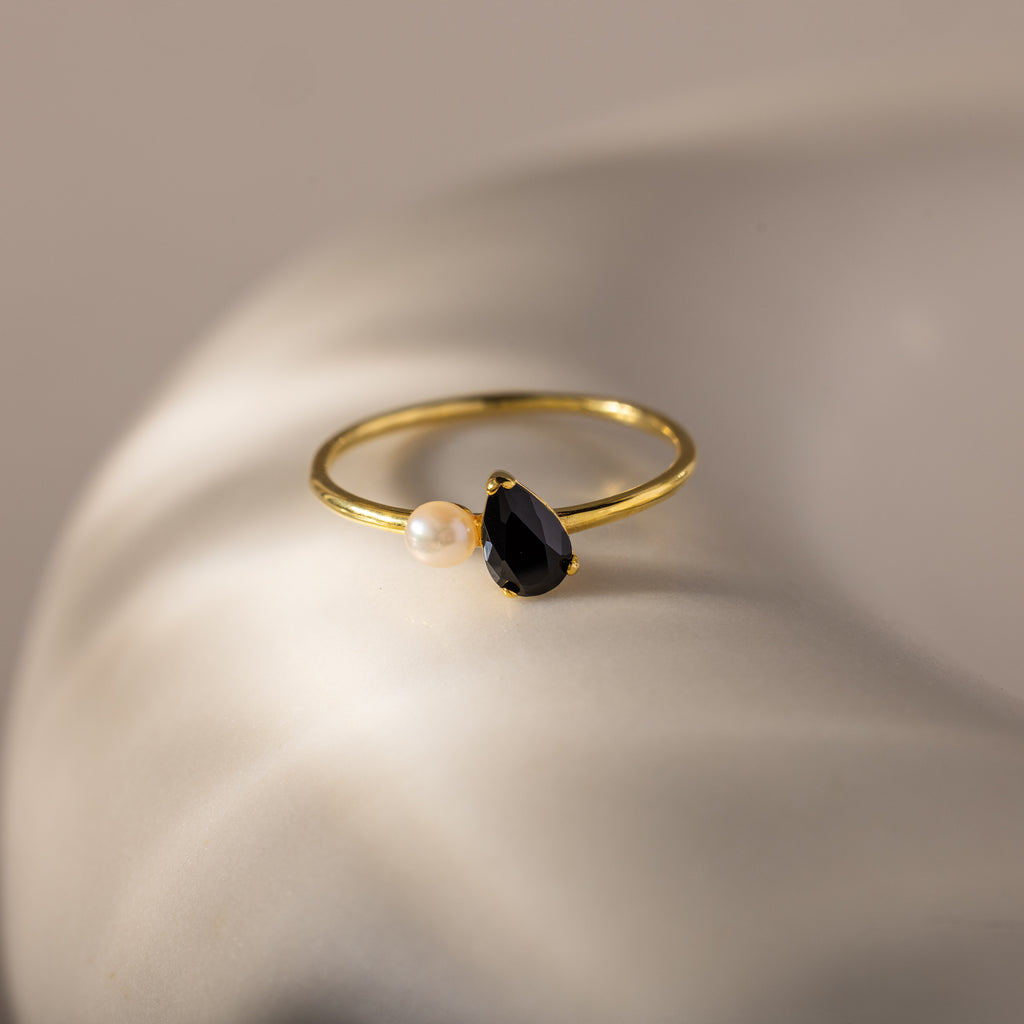 The Teardrop Onyx & Pearl Ring, featuring a black teardrop onyx and a lustrous pearl, rests on a smooth white surface, showcasing the essence of elegant jewelry.