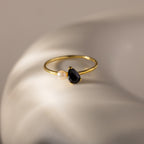 The Teardrop Onyx & Pearl Ring, featuring a black teardrop onyx and a lustrous pearl, rests on a smooth white surface, showcasing the essence of elegant jewelry.