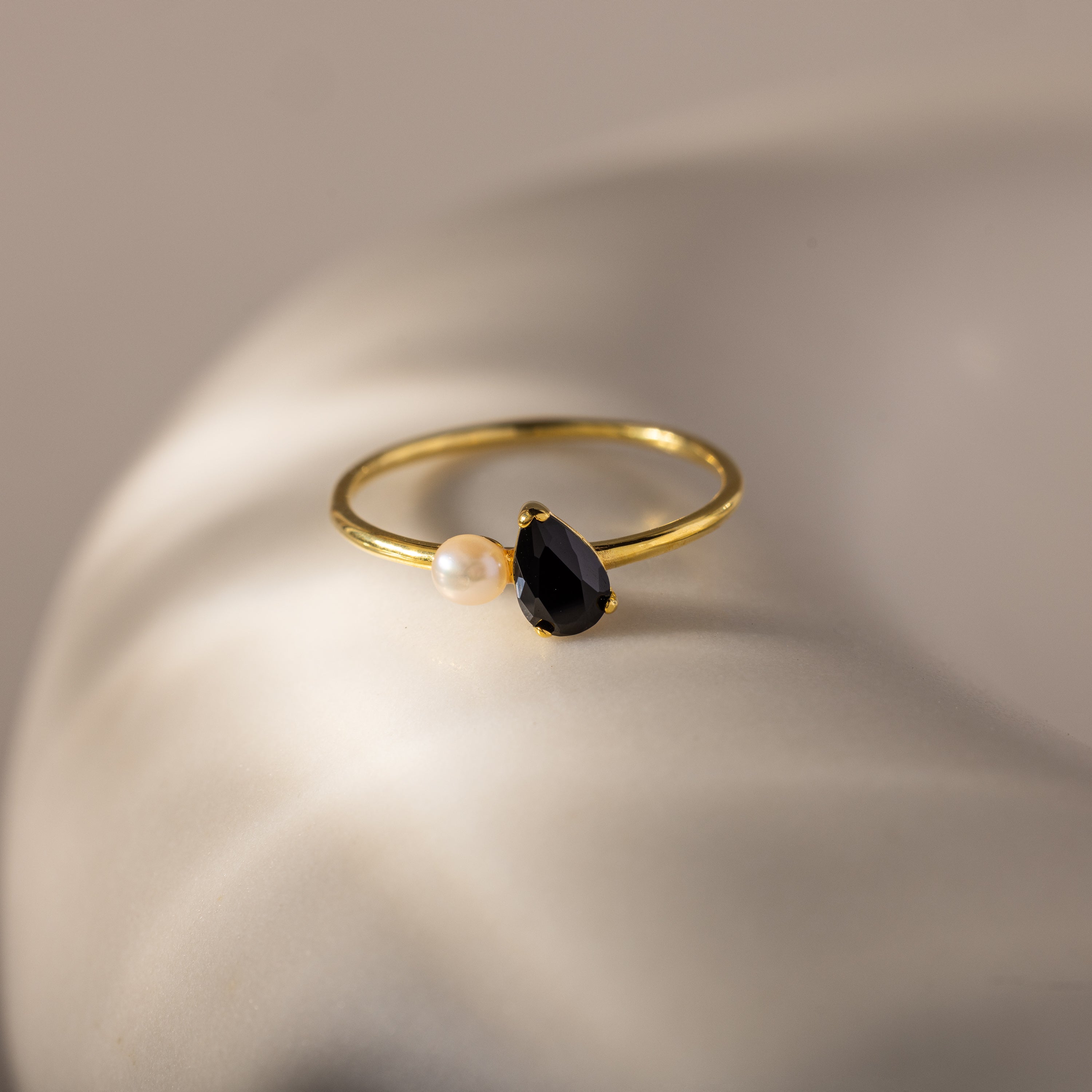 The Teardrop Onyx & Pearl Ring, featuring a black teardrop onyx and a lustrous pearl, rests on a smooth white surface, showcasing the essence of elegant jewelry.
