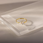 The Teardrop Opal & Pearl Ring, featuring a radiant pearl and opal gemstone, rests on a clear angled acrylic surface—a stunning piece of elegant jewelry.