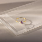 Teardrop Alexandrite & Pearl Ring: Gold ring with a teardrop alexandrite birthstone and a small white pearl, beautifully displayed on a clear, angled acrylic surface.